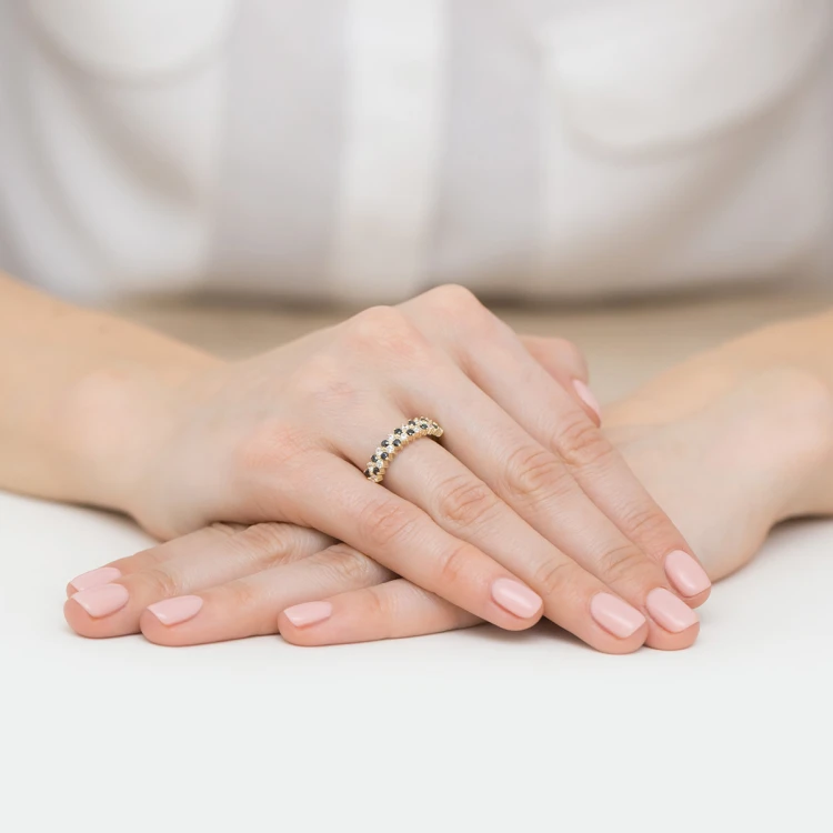 Złoty pierścionek z białymi i czarnymi cyrkoniami z kolekcji Kleur, prezentowany na dłoni z jasnoróżowym manicure, na białym tle produktu EP039-333
