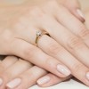 Elegancki pierścionek z żółtego złota z jednym brylantem prezentowany na dłoni z jasnoróżowym lakierem do paznokci produktu W0222.B3.DIW.10