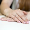 Złoty pierścionek z białym kamieniem, prezentowany na dłoni z różowym manicure na jasnym tle, produktu W0181.Z3.DIW.01